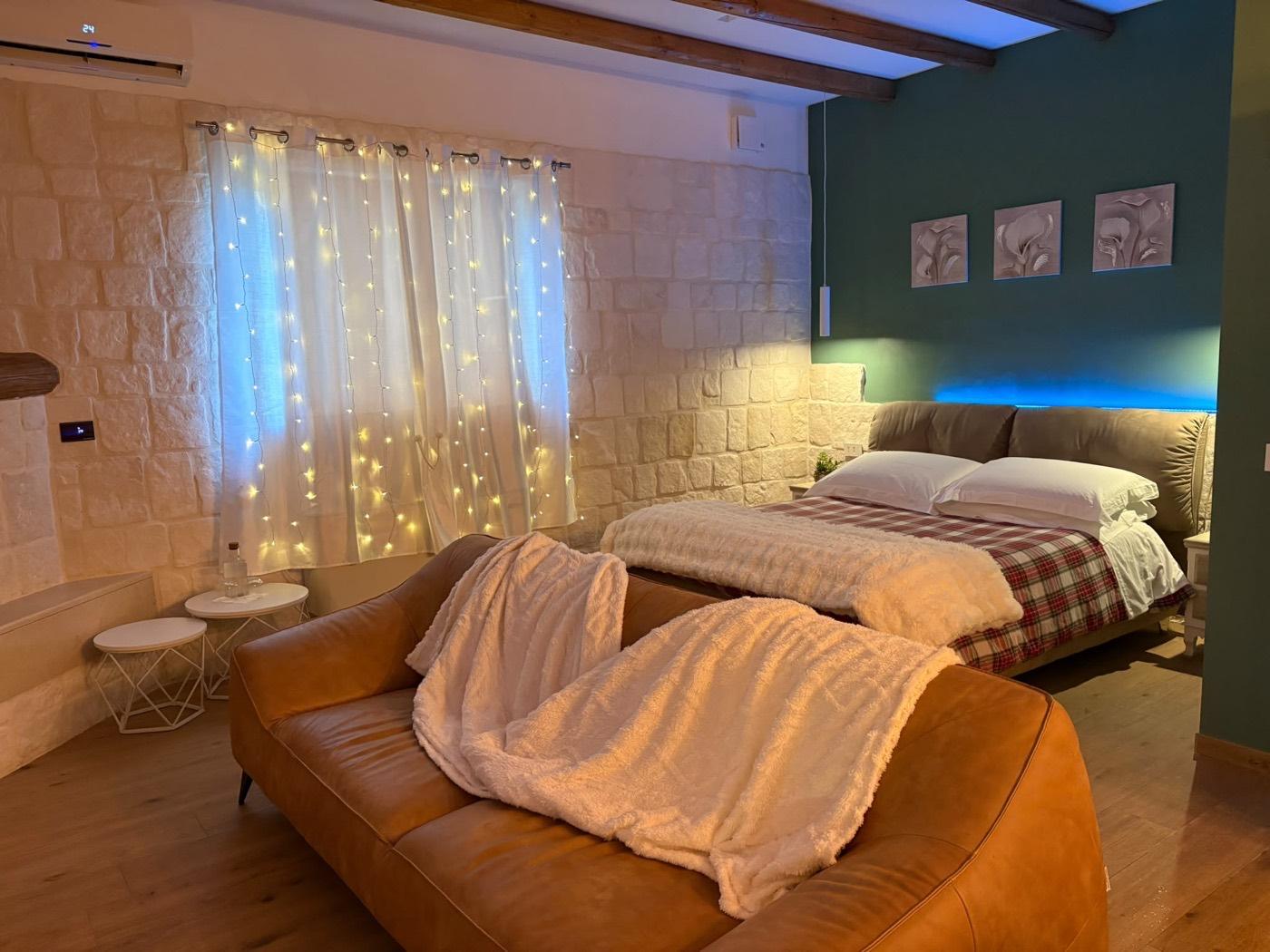 Junior Suite Deluxe del B&B Villa Cassandra con letto matrimoniale, divano in pelle e parete in pietra